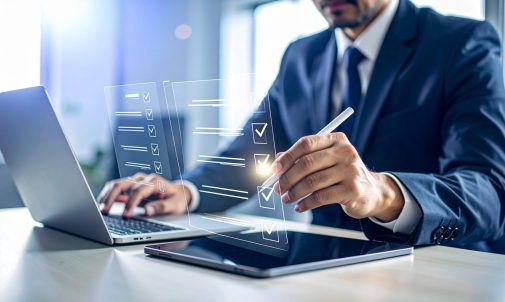 Businessman completes digital checklist on tablet with laptop, modern office setting